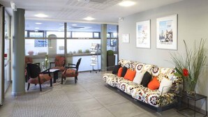 A reception area with a sofa, chairs, a reception desk, and framed pictures on the wall. - Nemea Appart’Hotel Toulouse Constellation (Toulouse)