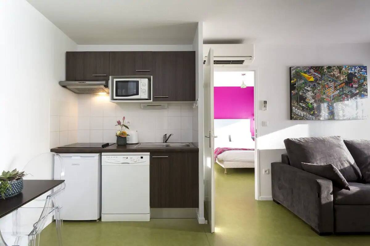 Een compacte keuken met een magnetron, vaatwasser en een eethoek met een tafel en stoelen.