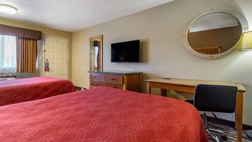 Quarto de hotel com duas camas, uma escrivaninha, uma cadeira, televisão, espelho e porta.