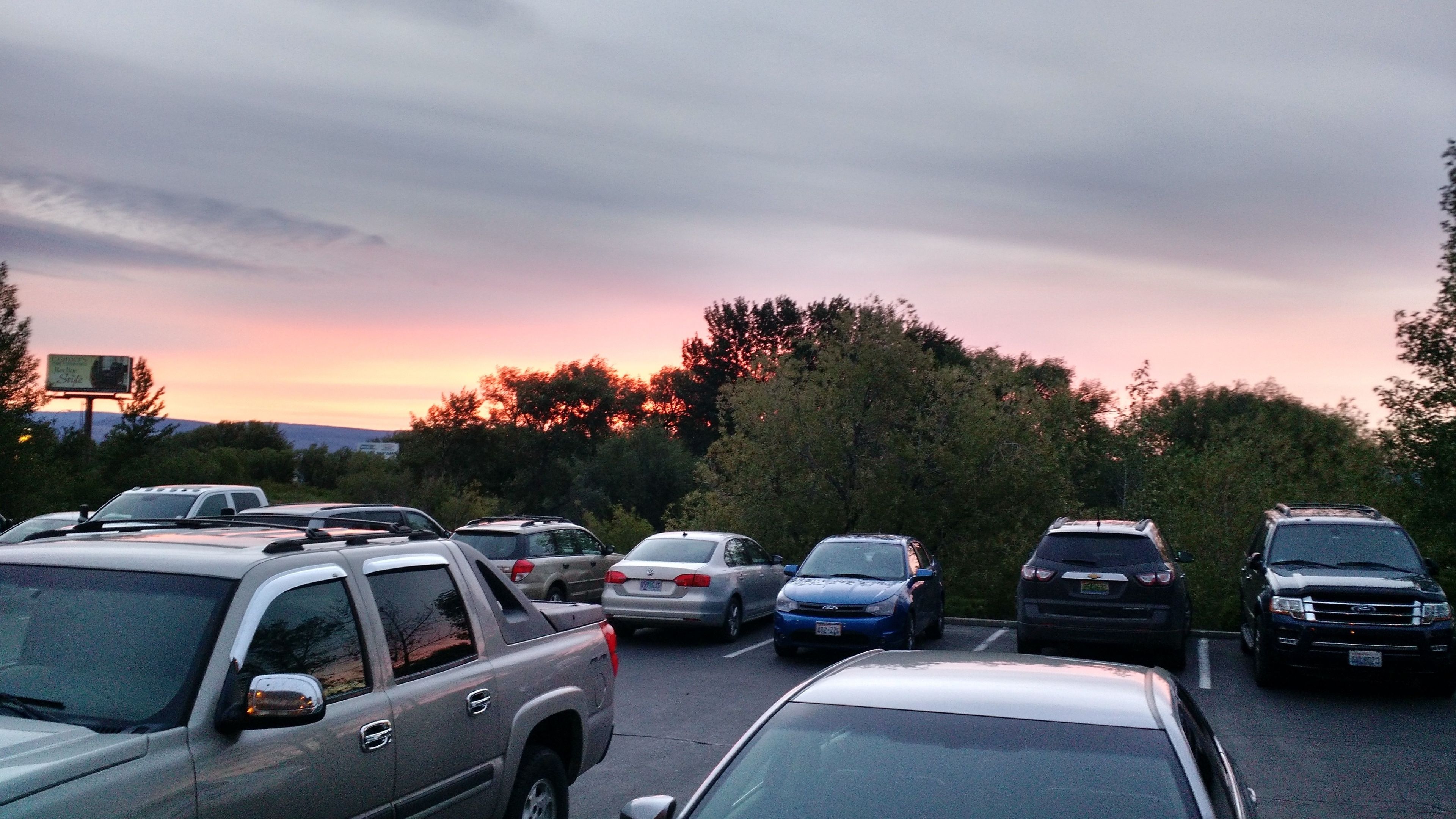 A parking lot with several cars and a billboard in the background.