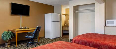 Habitación de hotel con dos camas, un escritorio con silla, un refrigerador, un televisor montado en la pared y una planta.