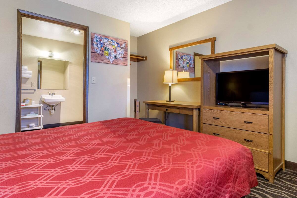 Une chambre d’hôtel avec un lit, un bureau avec une télévision, un miroir, une lampe et un mur orné d’une carte.