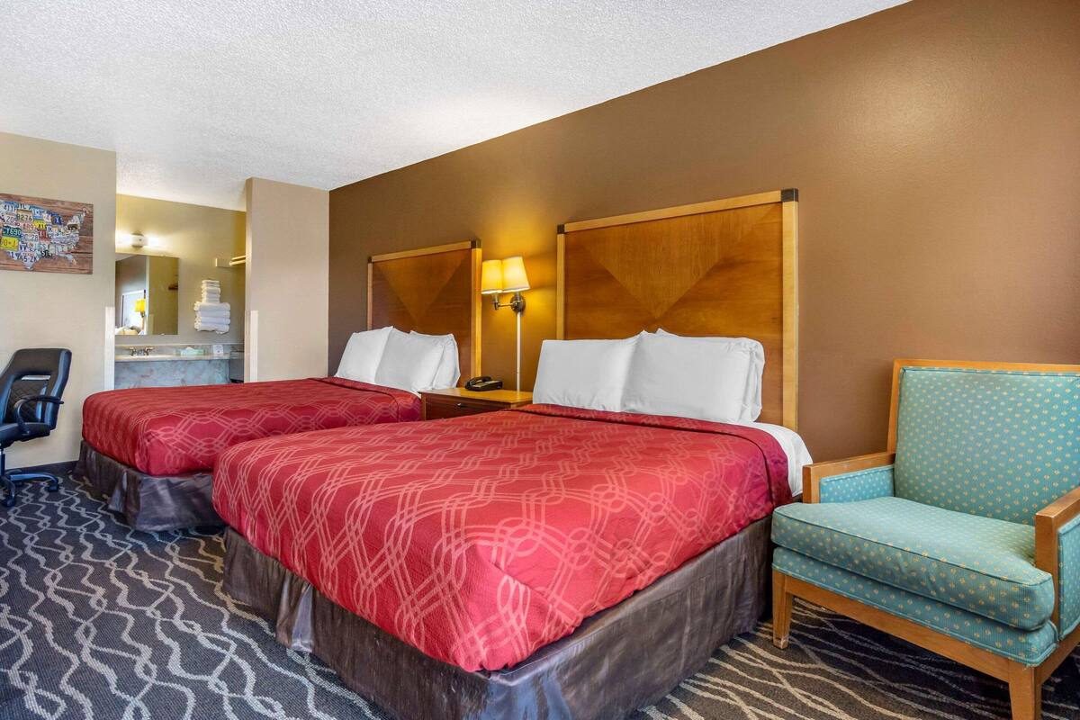 Une chambre d’hôtel avec deux lits, un bureau, une chaise et une salle de bain visible à travers une porte.