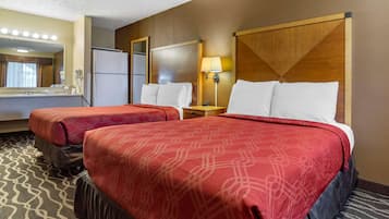 Camera d'albergo con due letti, un frigorifero, uno specchio, una lampada e pavimento tappezzato.