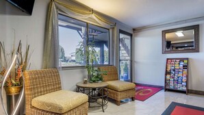 A hotel lobby with wicker furniture, a small table, a potted plant, a bulletin board, and a large window with a view.