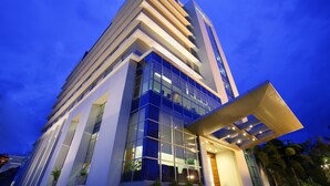 A modern hotel with a prominent glass facade, a flat roof, and a vertical entrance. - Hotel Santika Makassar (Makassar)