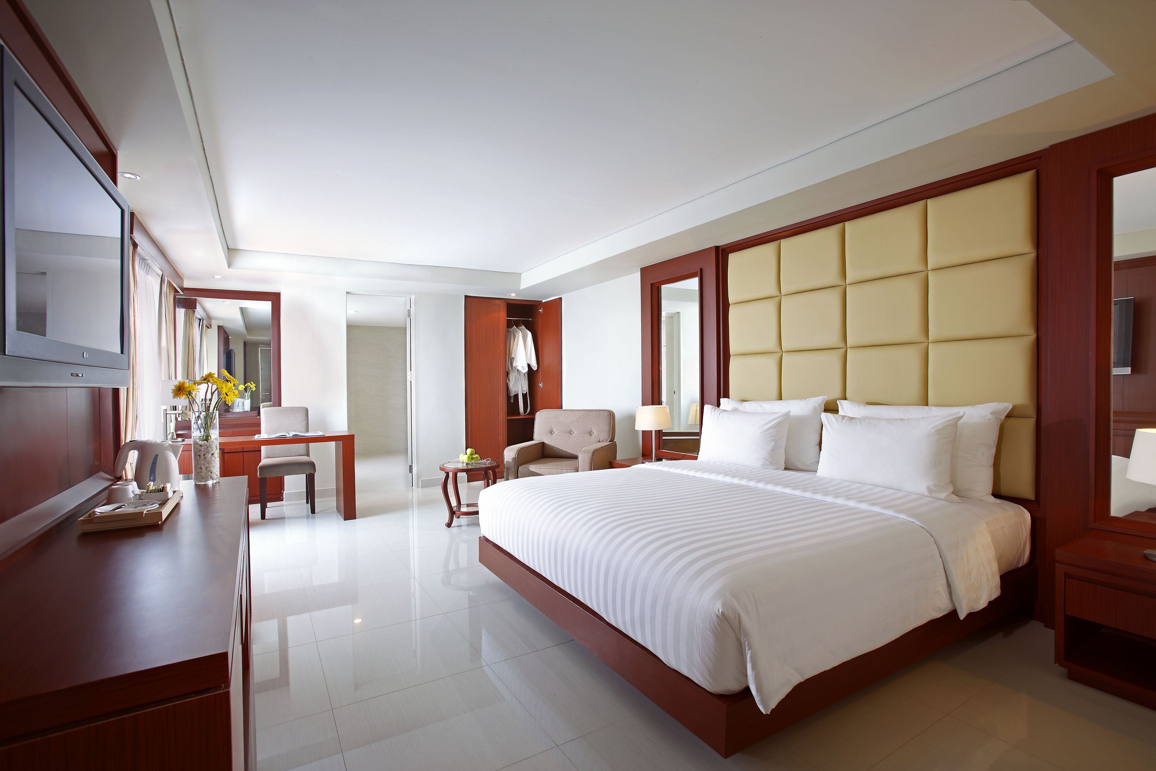 A modern hotel room with a large bed, a desk, a chair, a TV, and a wardrobe.