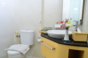 A modern bathroom with a white toilet, a sink with a vase of flowers, and a mirror above the sink. - Hotel Santika Makassar (Makassar)