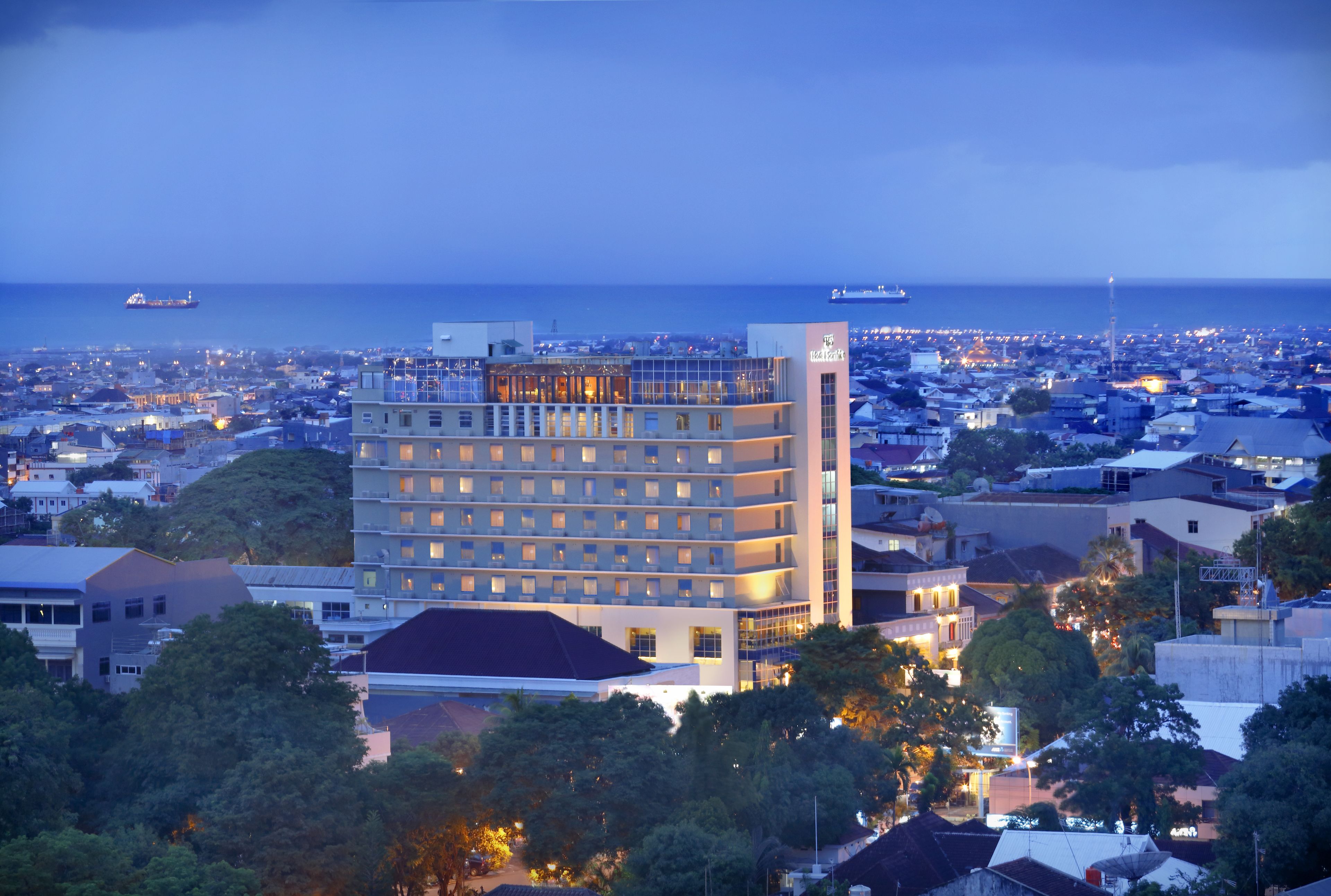 A multi-story hotel with a prominent corner tower, surrounded by dense urban development and a view of the sea.
