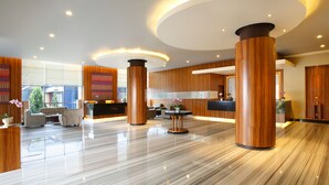 A modern lobby with wooden accents, a reception desk, seating area, and large windows. - Hotel Santika Makassar (Makassar)