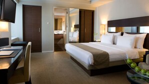 A hotel room with a bed, desk, chair, television, and a glass table with apples. - Hotel Santika Makassar (Makassar)