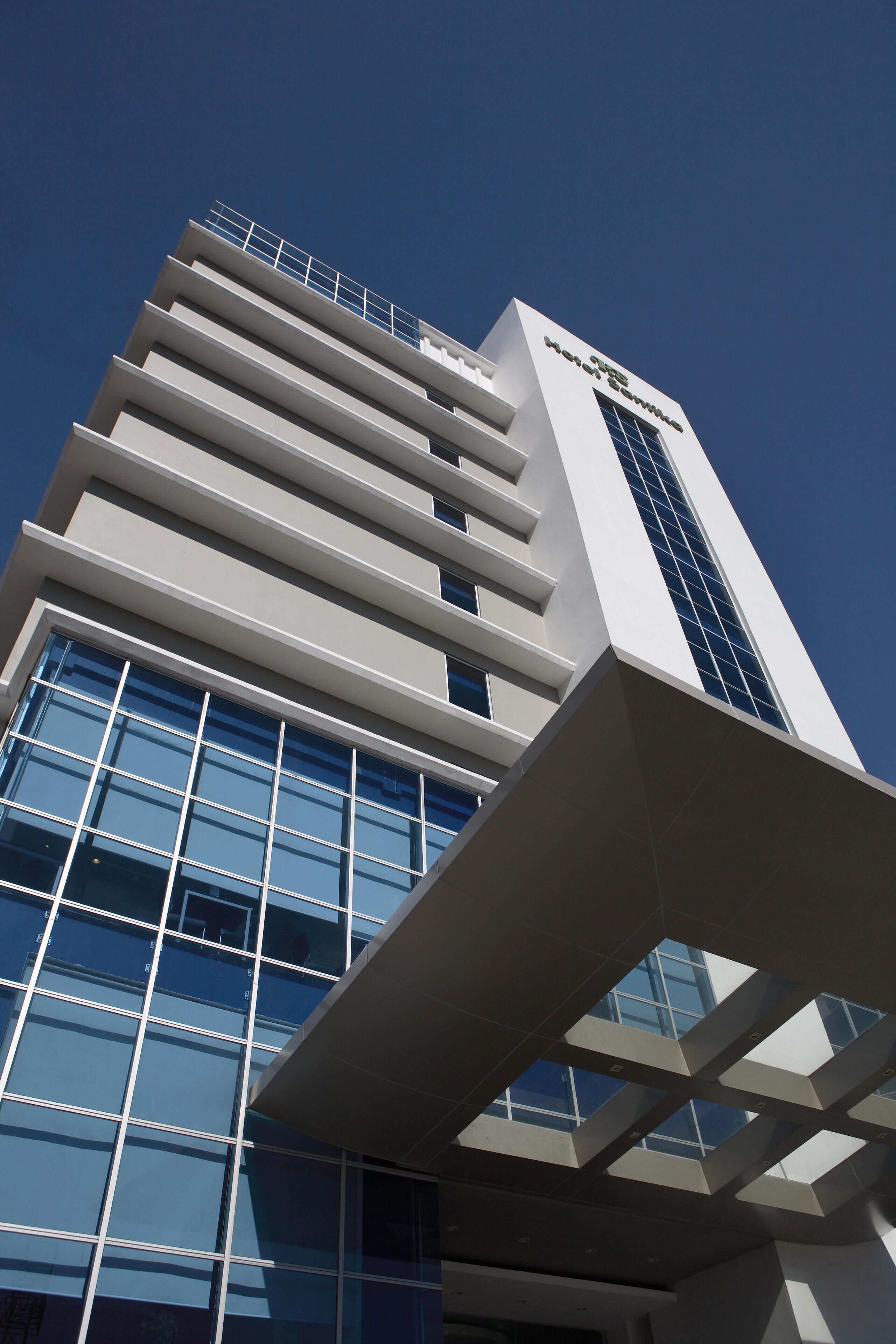 A modern hotel building with a prominent glass facade and a clear sky.