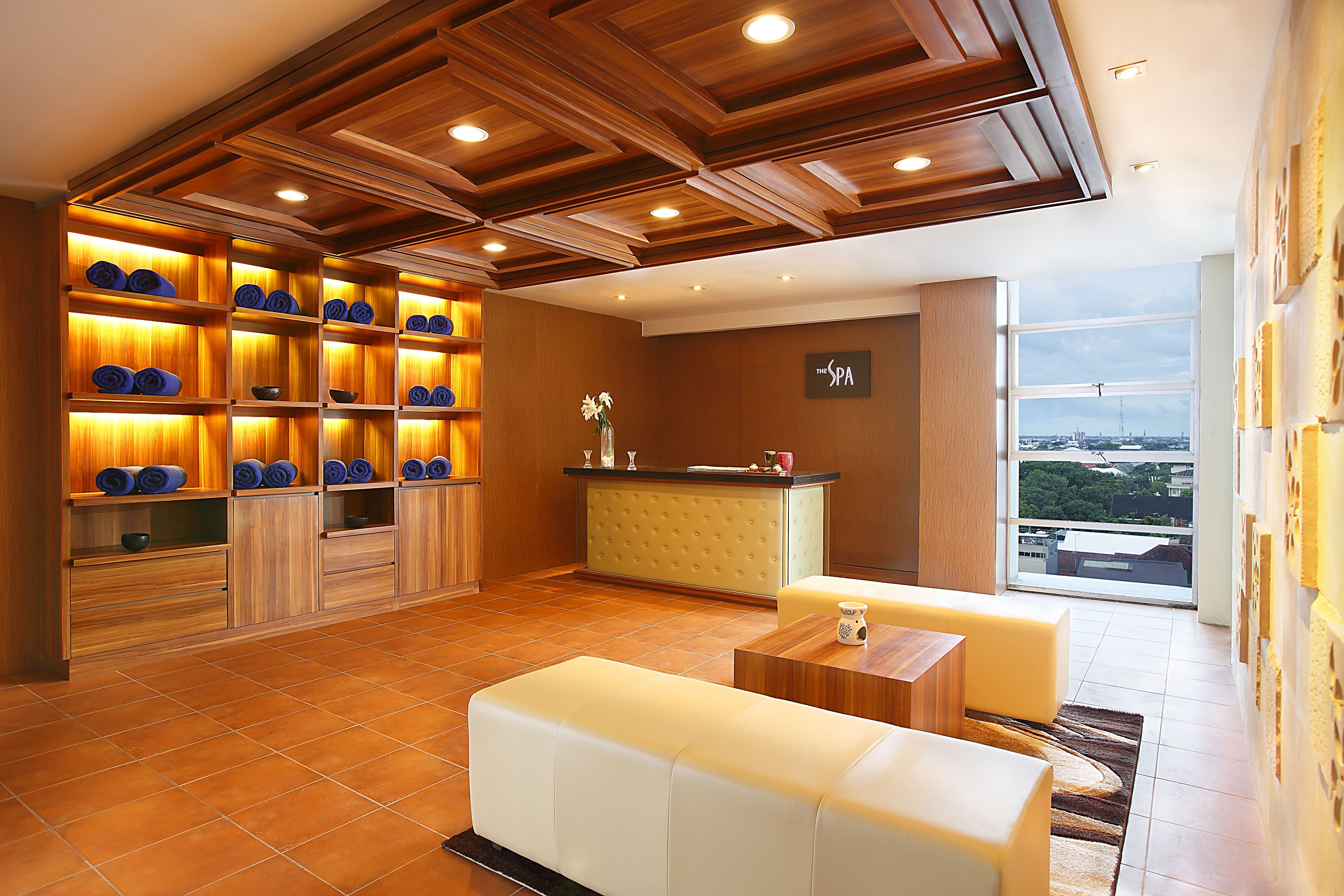 A spa reception area with a wooden ceiling, a reception desk, and a view of the city through large windows.
