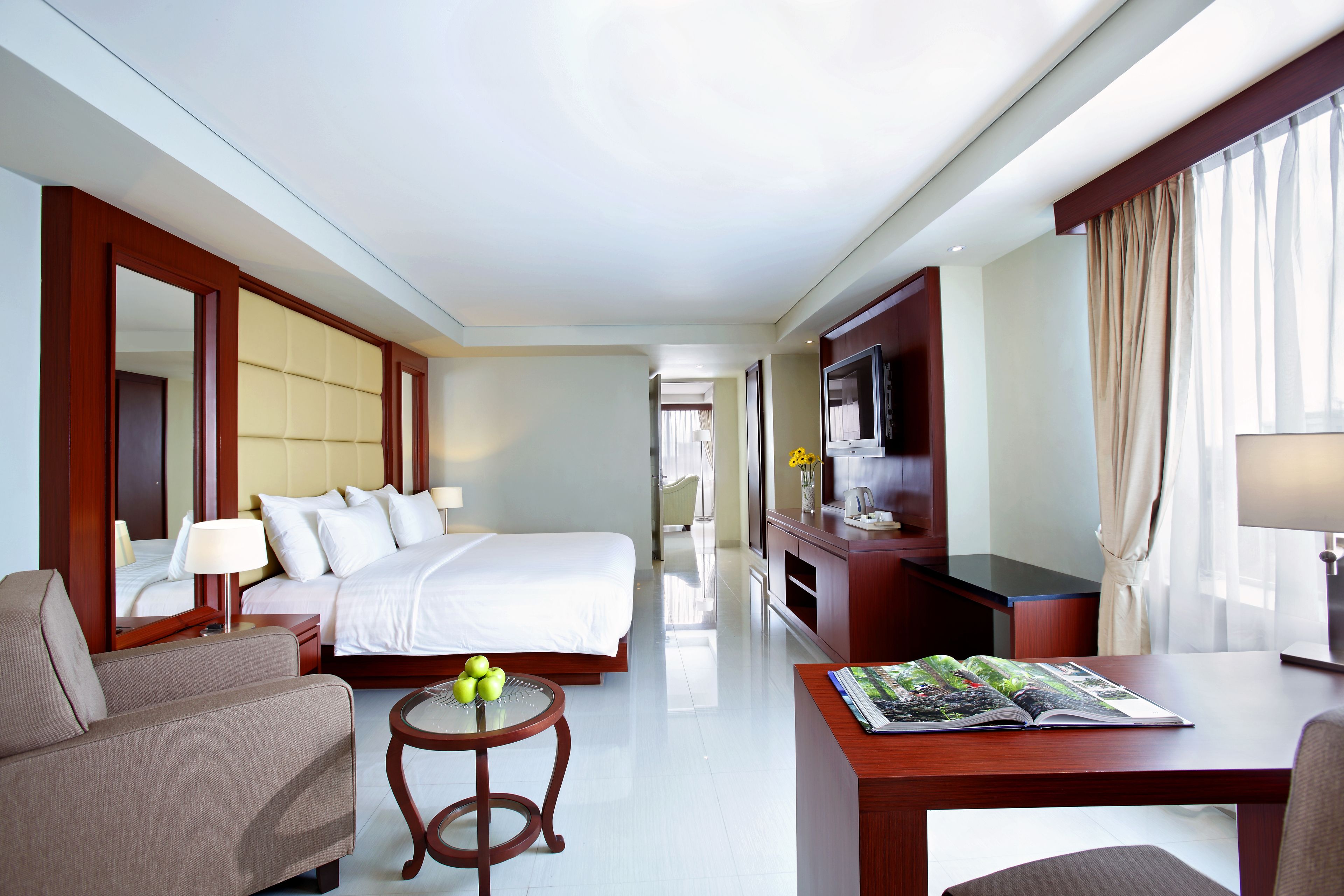 A hotel room with a bed, a sofa, a small table with apples, a TV, and a desk with a magazine.