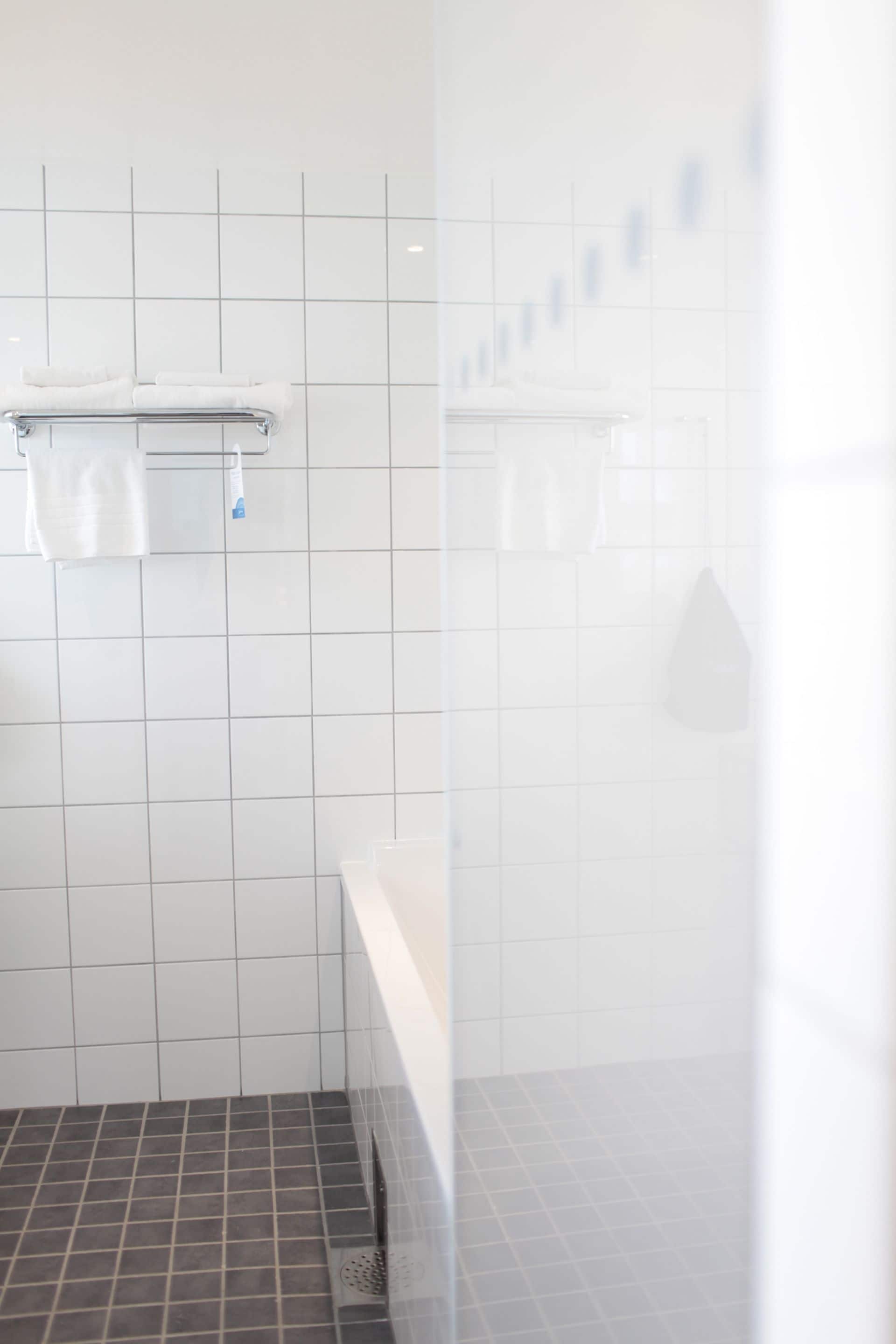 A bathroom with white tiled walls, a grey floor, and a white countertop with a towel rack.