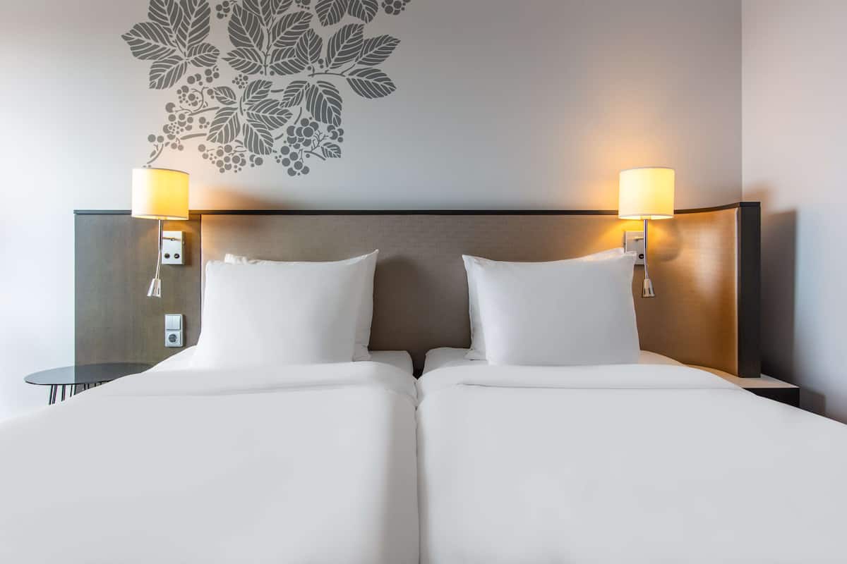 A hotel room with a double bed, two bedside lamps, and a wall decal of leaves.
