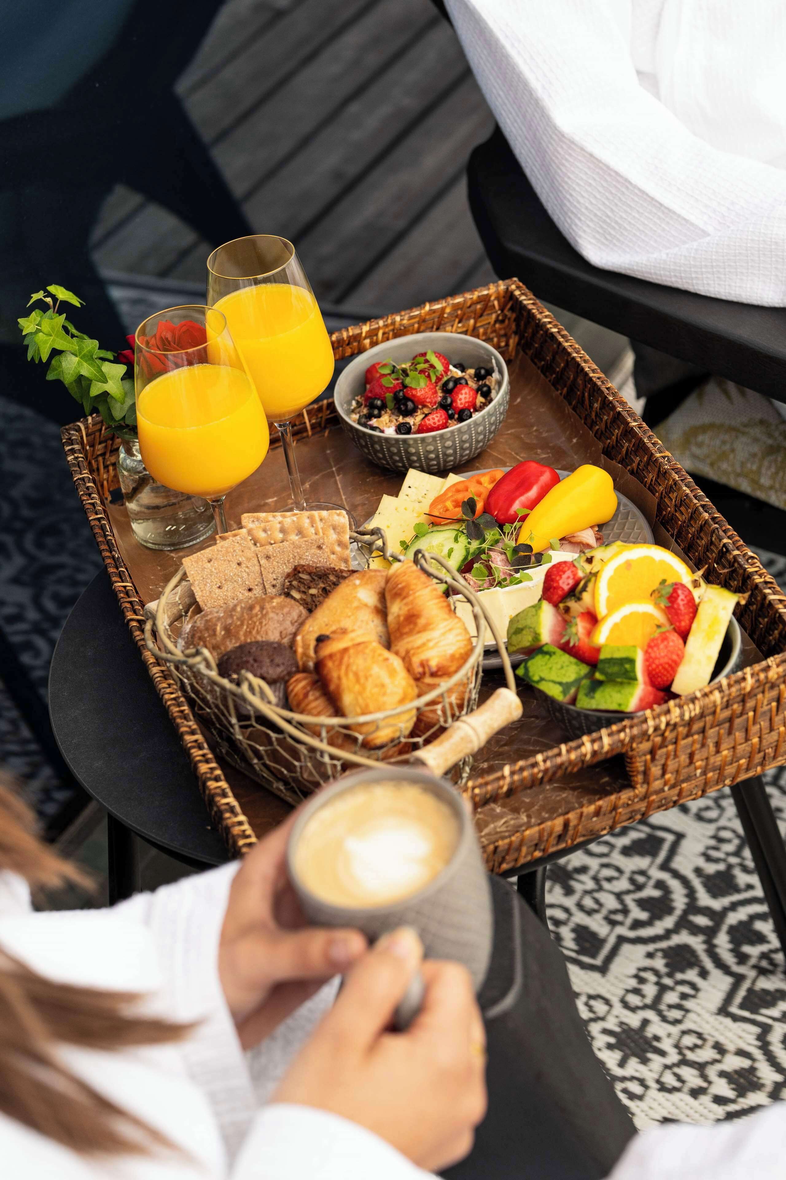 Un plateau de petit-déjeuner avec des croissants, du pain, des fruits et du jus, posé sur une table.