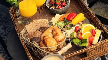 Un plateau de petit-déjeuner avec des croissants, du pain, des fruits et du jus, posé sur une table.