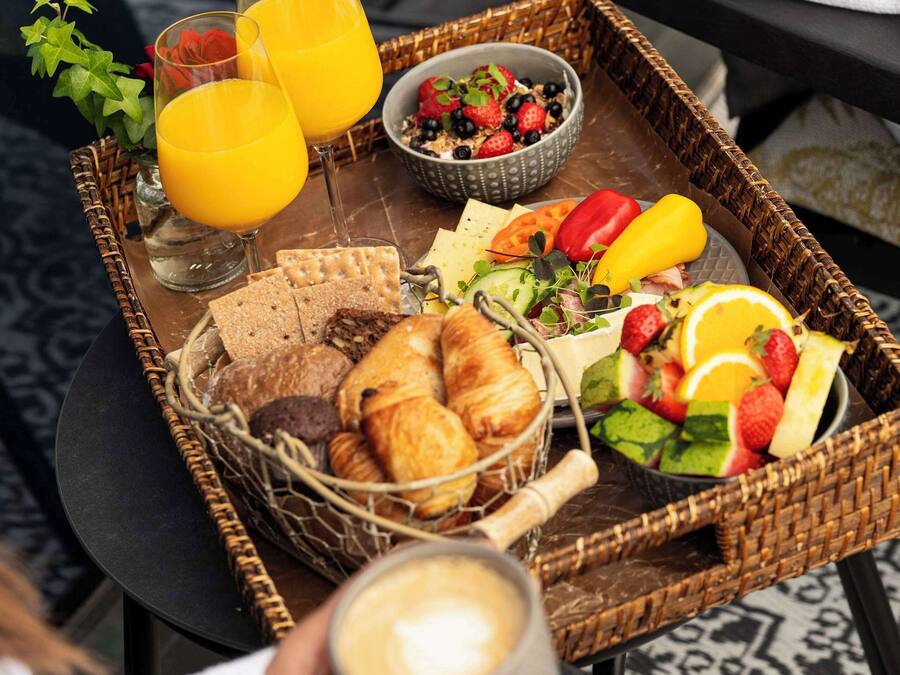 Un plateau de petit-déjeuner avec des croissants, du pain, des fruits et du jus, posé sur une table.
