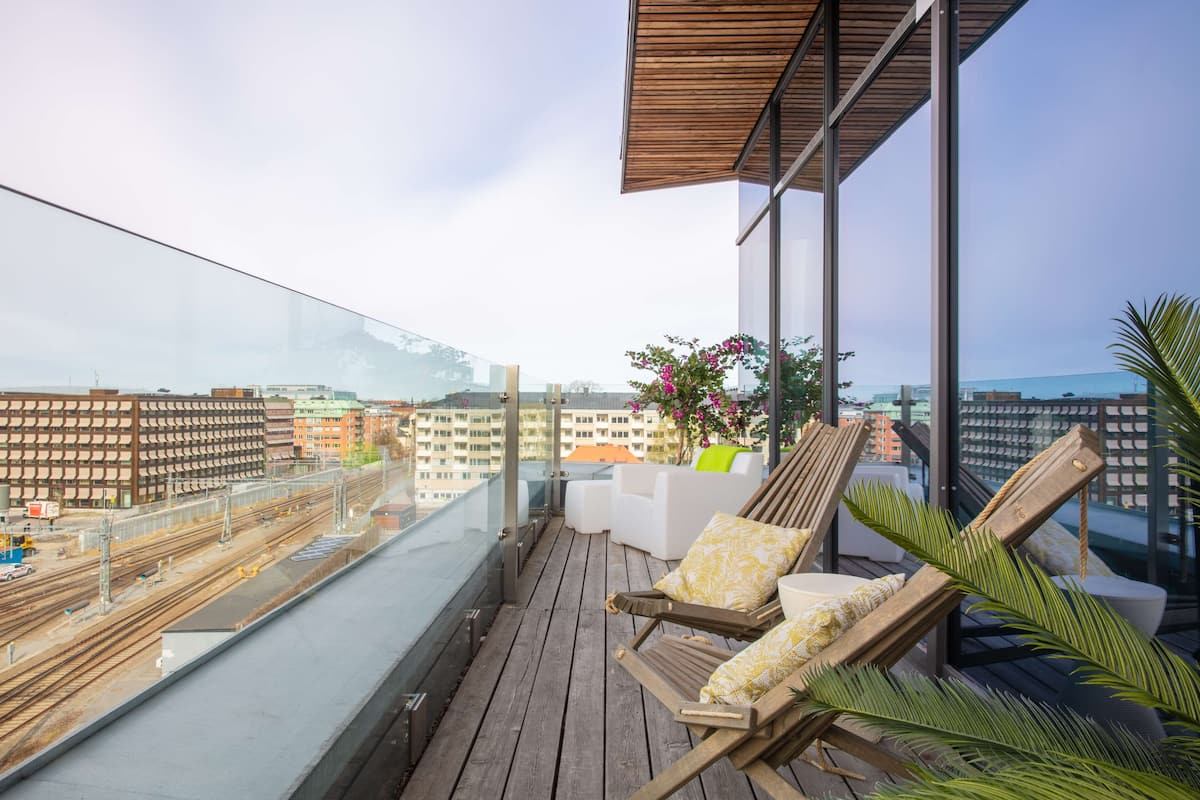A balcony with wooden flooring, two lounge chairs, a white sofa, and a potted plant.