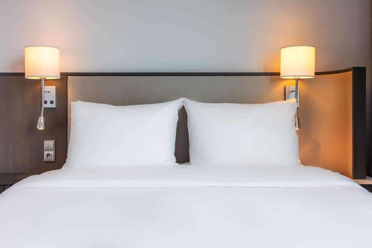 A hotel room with a neatly made bed, two wall-mounted lamps, and a control panel on the wall.