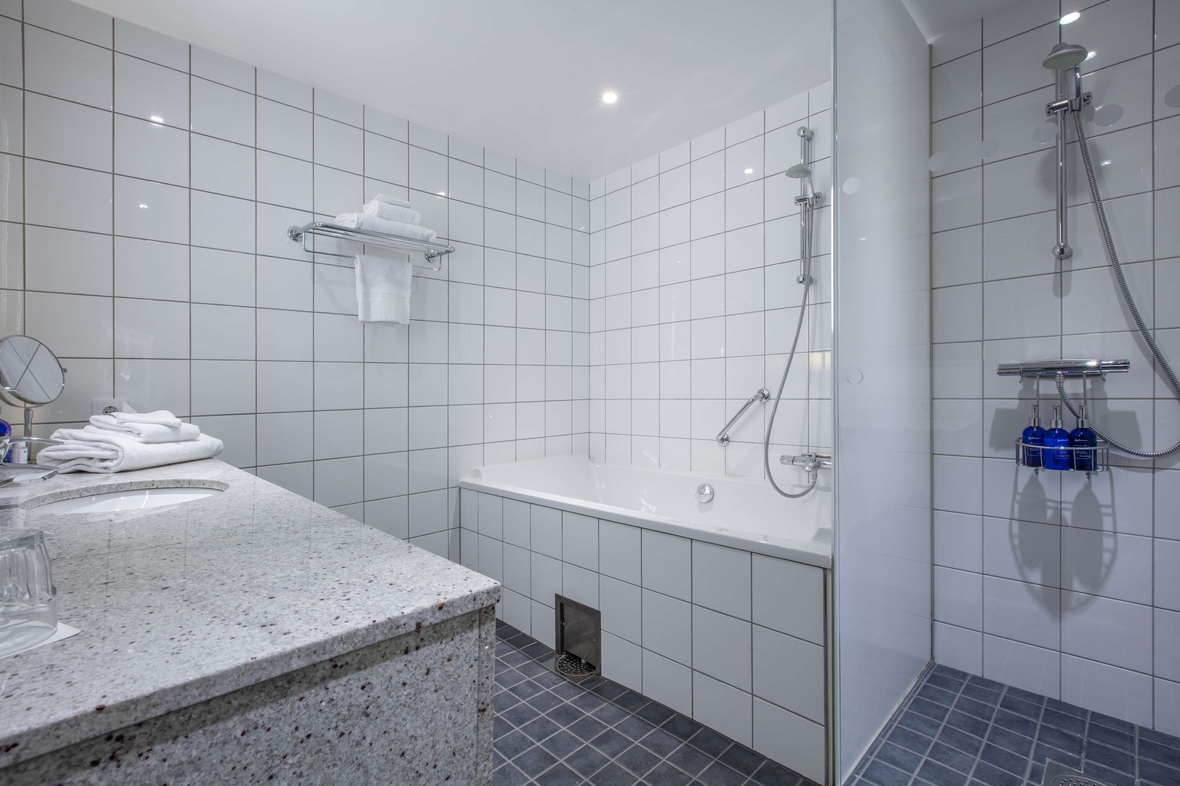 A modern bathroom with a large bathtub, a shower area, and a granite countertop with a sink and mirror.