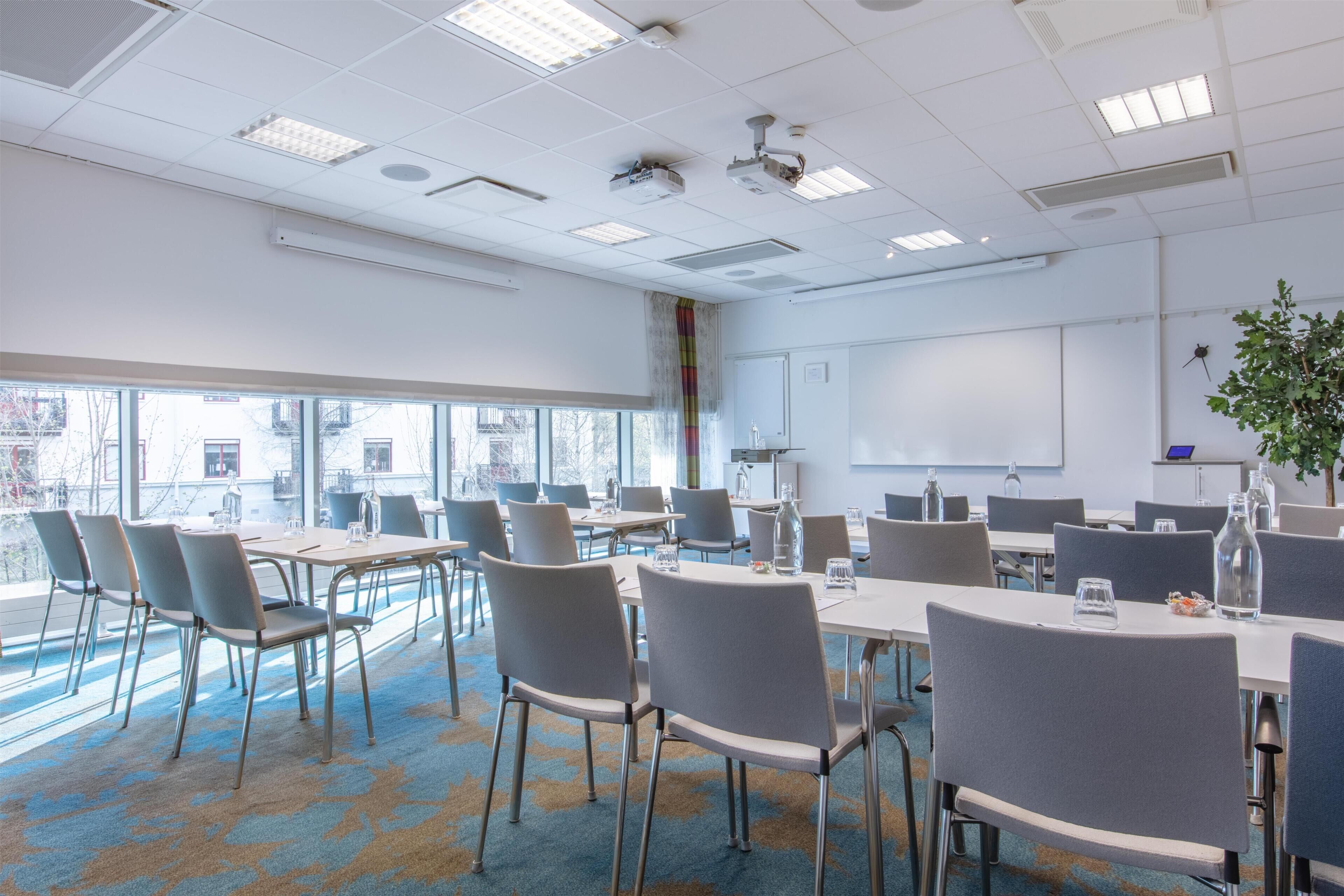 A conference room with tables, chairs, a projector, and a large window.