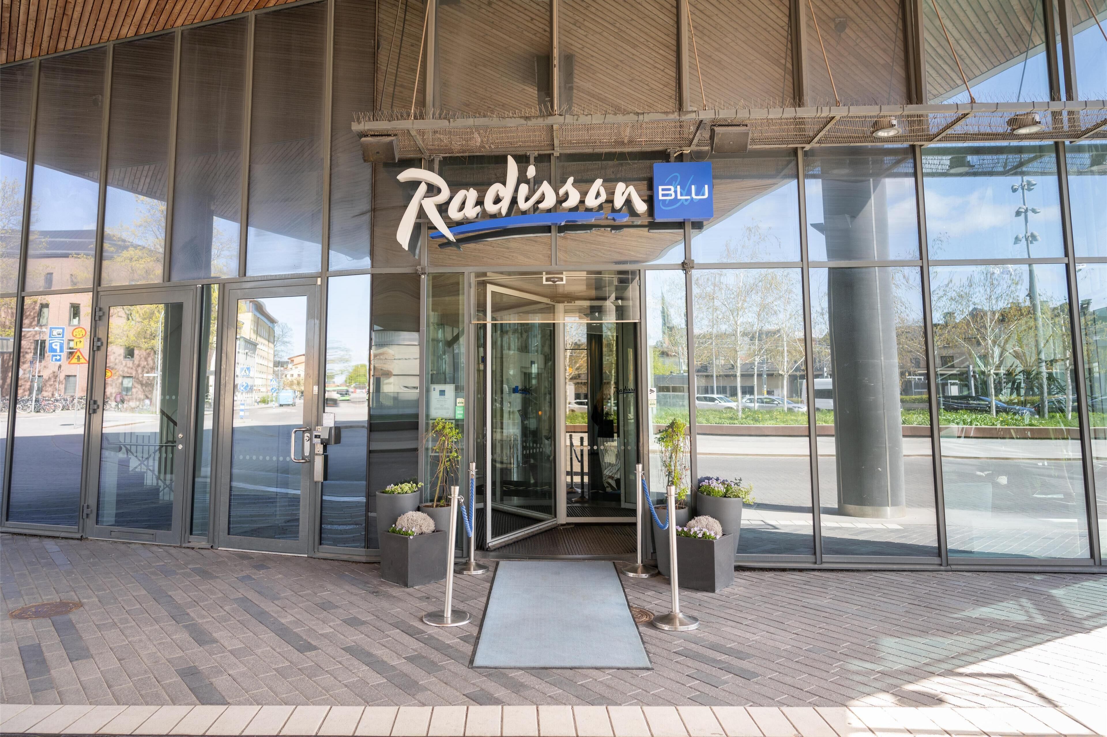 La entrada del hotel Radisson Blu con puertas de vidrio, un letrero azul y plantas en macetas.