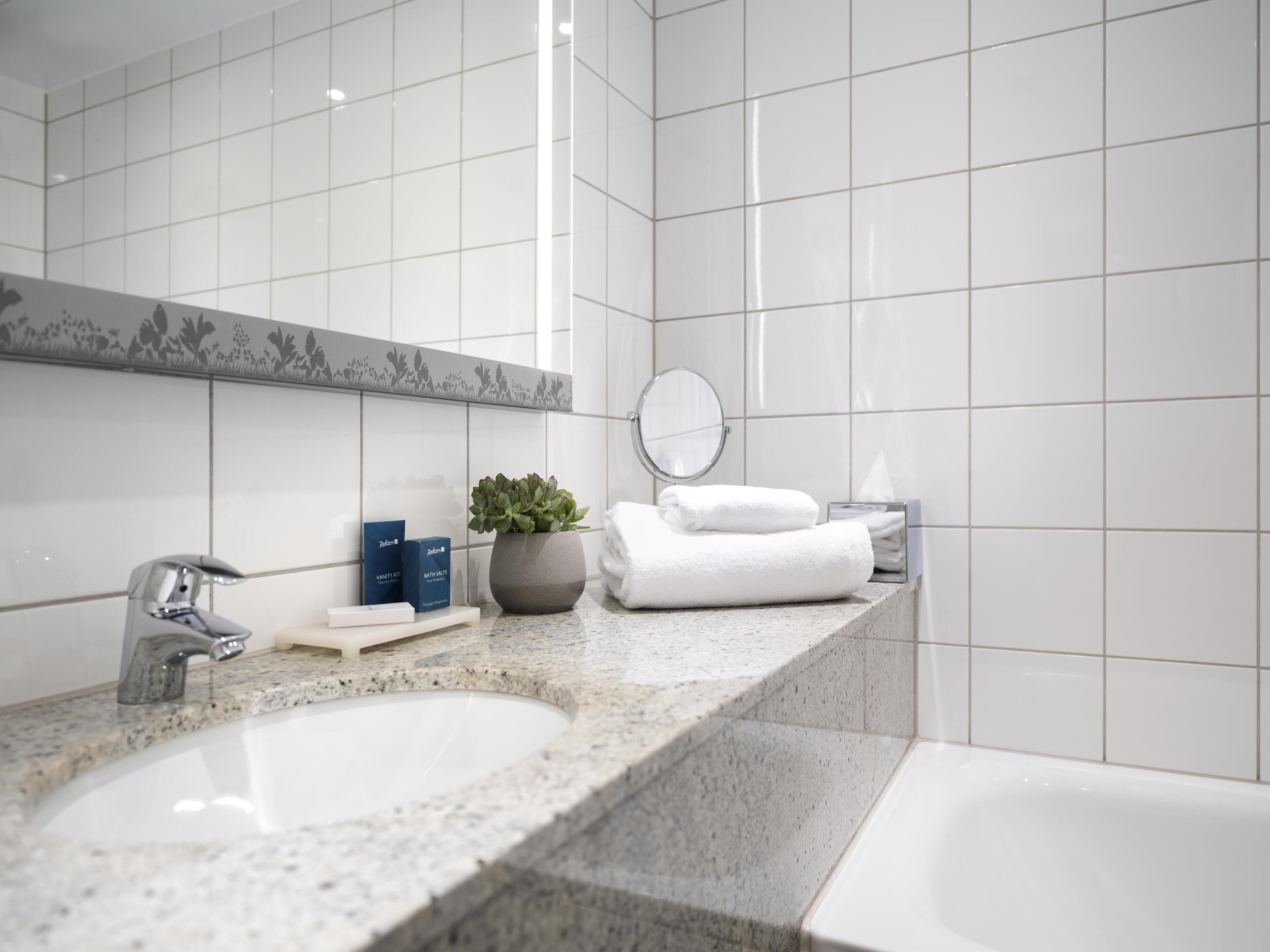 Un baño moderno con dos lavamanos, un espejo grande, una planta en maceta y toallas dobladas con cuidado.