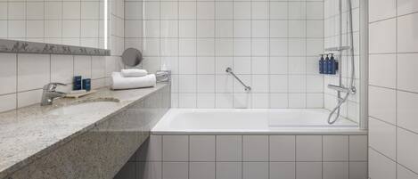 Un baño moderno con encimera de granito, azulejos blancos, bañera, ducha y retrete.
