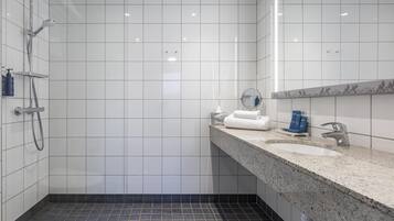 Une salle de bain moderne avec des carreaux blancs, une douche, un lavabo doté d’un plan de travail en granit et un miroir.
