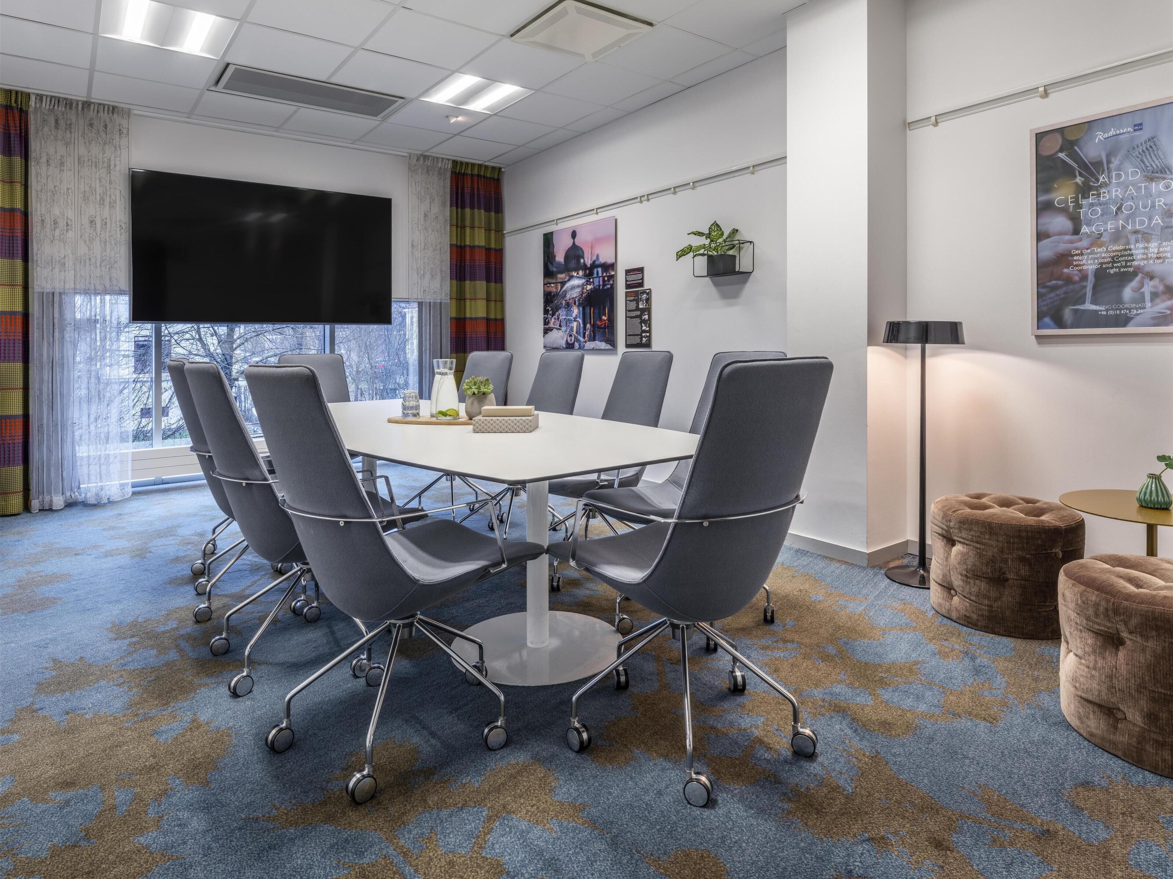 A conference room with a large table, grey chairs, a TV, and a window with a view.