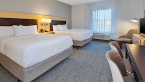 Habitación de hotel con dos camas, un escritorio, una silla, una lámpara y un ventanal con cortinas.
