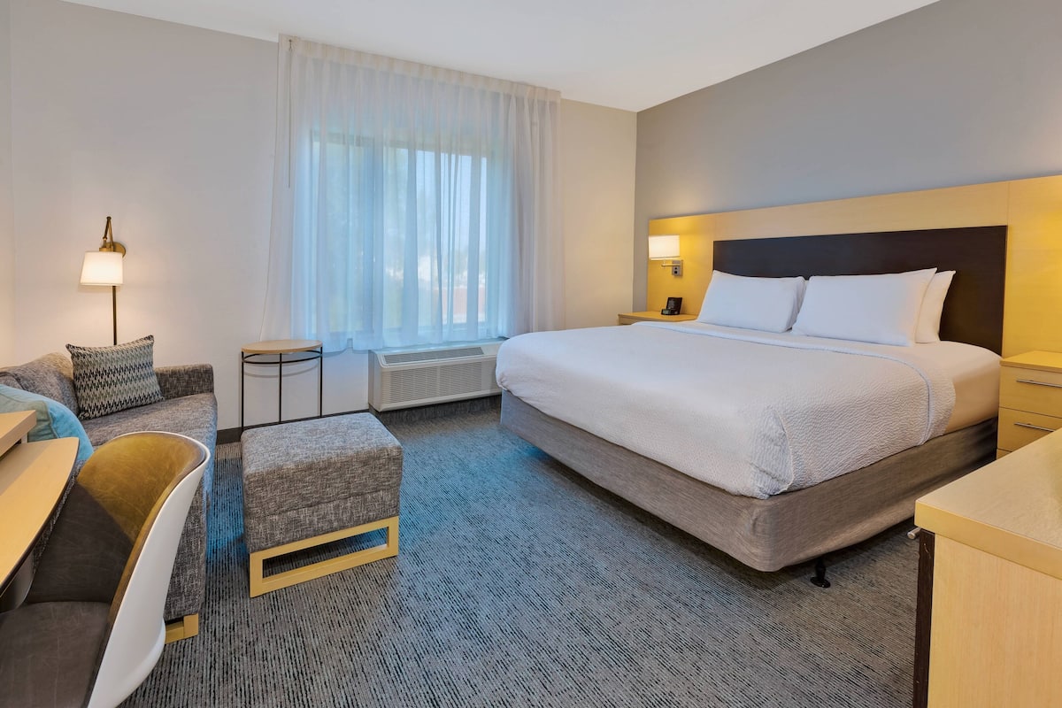 A hotel room with a large bed, a desk, a chair, a small table, and a window with curtains.