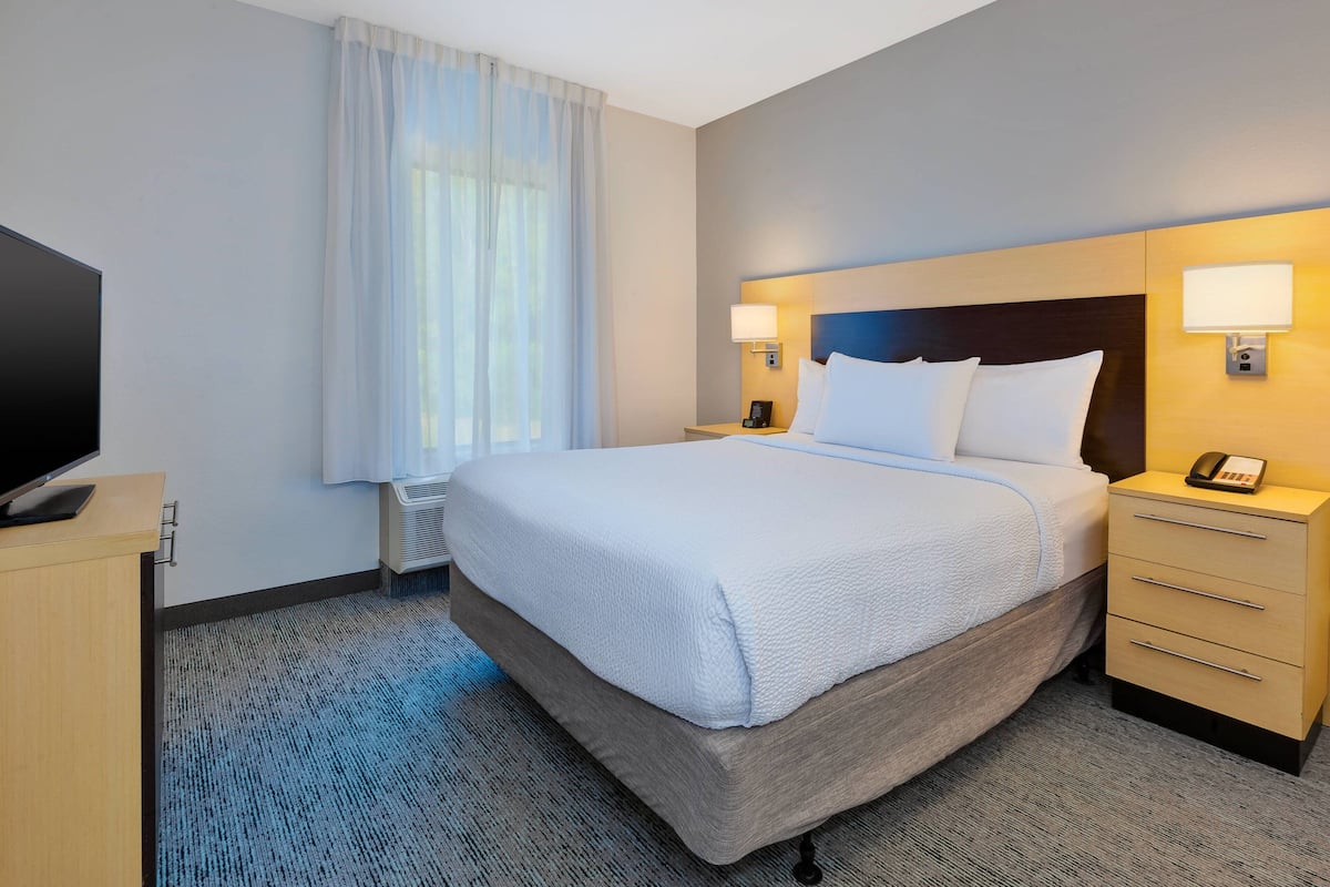 A hotel room with a large bed, bedside lamps, a flat-screen TV, and a desk with a telephone.