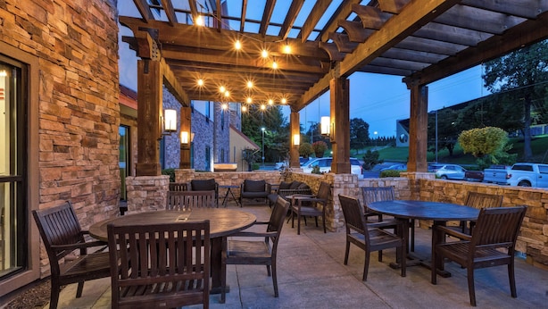 Un patio al aire libre con paredes de piedra, mesas y sillas de madera, y luces colgantes.