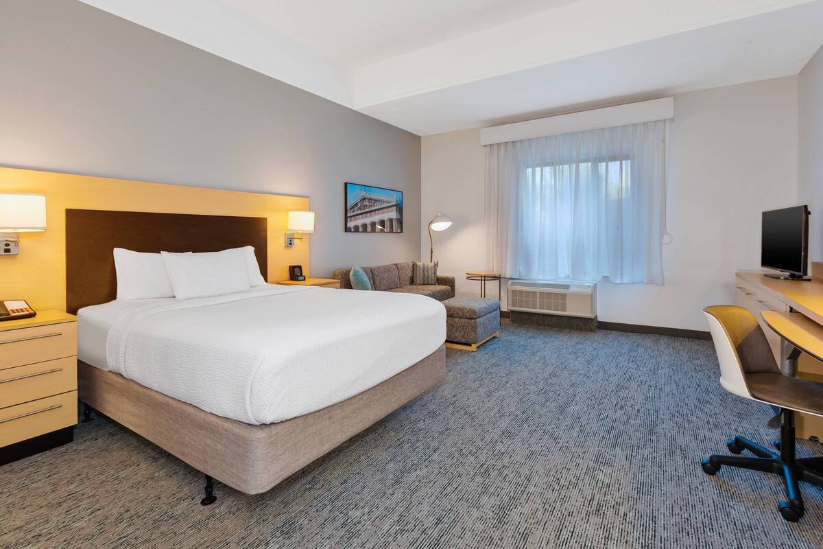 A hotel room with a large bed, a desk, a chair, a sofa, and a television.