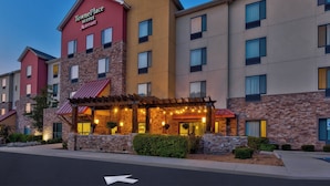Un hotel TownePlace Suites Marriott con fachada de piedra, varios balcones y un área exterior cubierta con luces colgantes.