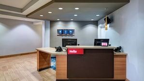 A hotel reception desk with a "Hello" sign, a flat-screen TV, and a digital information kiosk. - TownePlace Suites Monroe (Monroe)