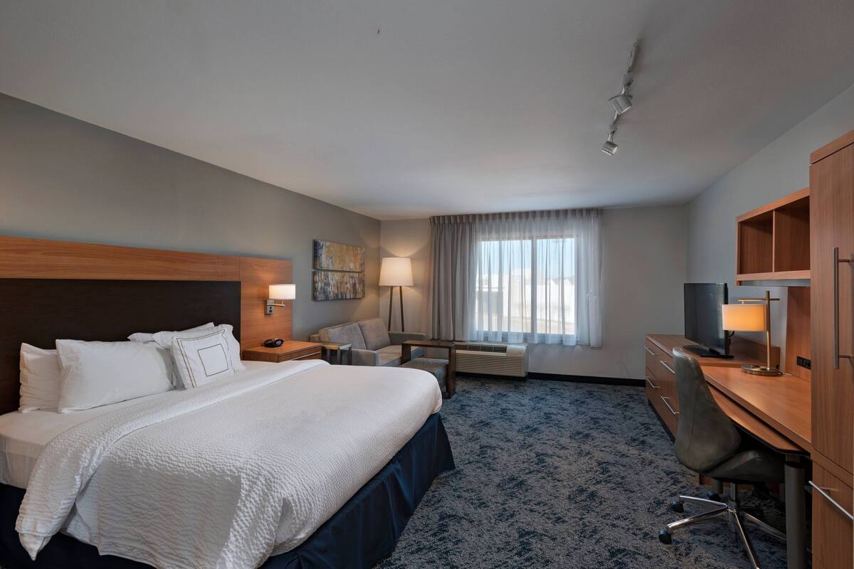 A hotel room with a large bed, a desk, a chair, a lamp, and a window with curtains.