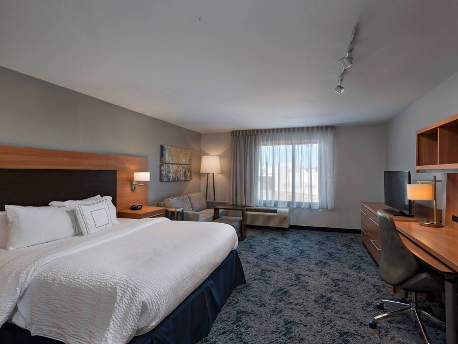 Una habitación de hotel con una cama grande, un escritorio, una silla, una lámpara y un ventanal con cortinas.