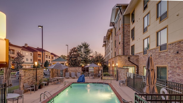 A pool area with a rectangular pool, lounge chairs, umbrellas, and a stone wall. - TownePlace Suites Monroe (Monroe)