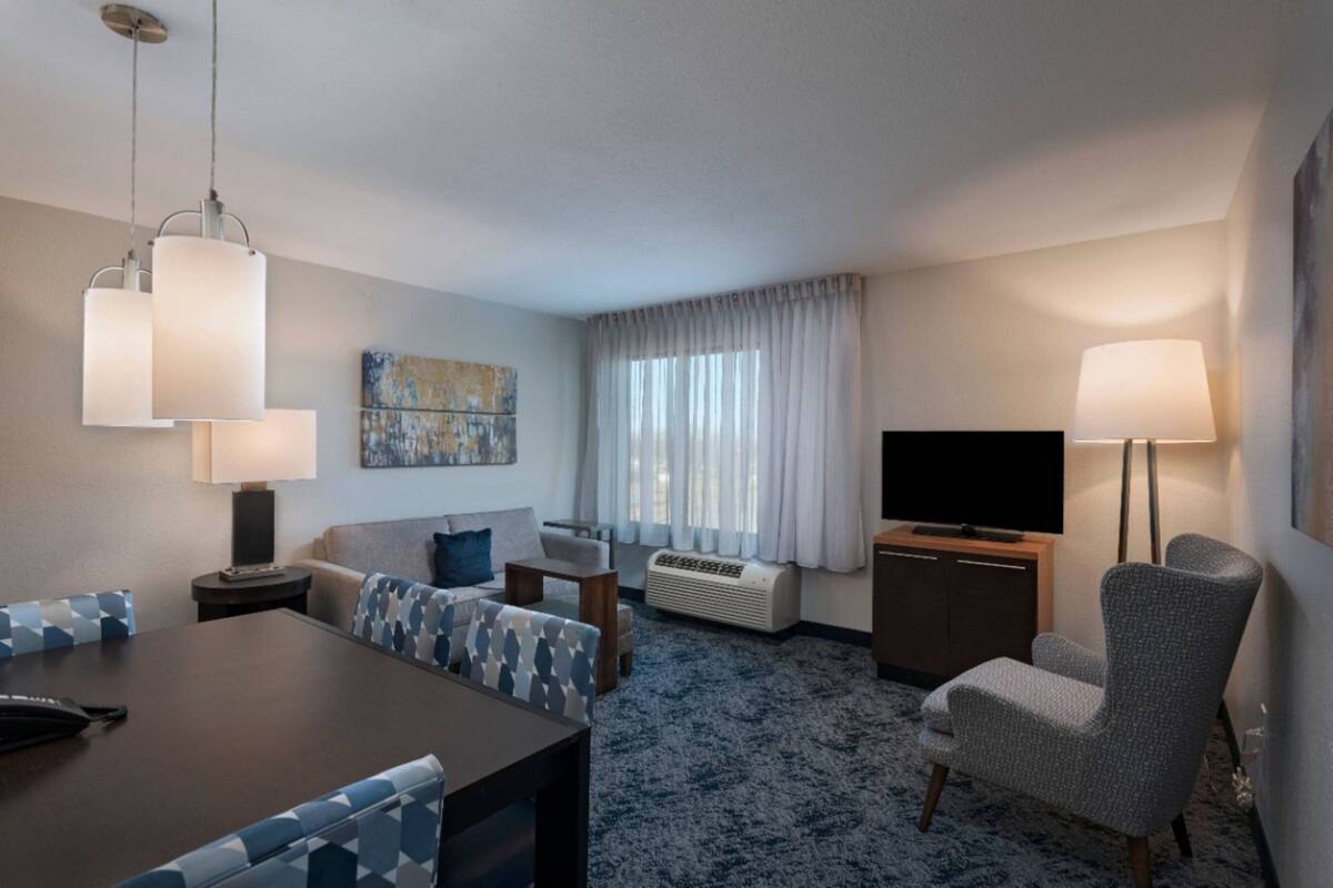 A hotel room with a dining table, sofa, TV, and lamp.