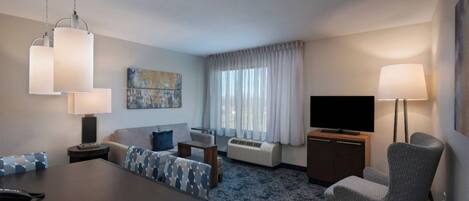 A hotel room with a dining table, sofa, TV, and lamp.