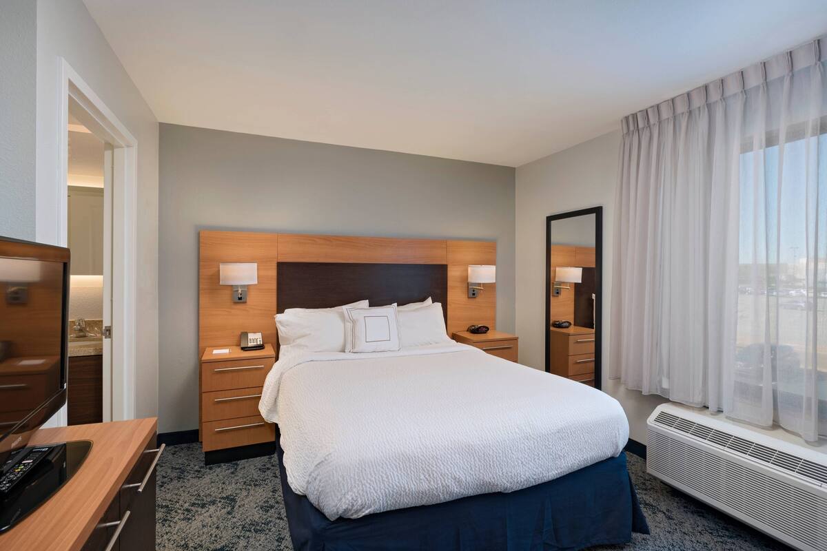 A hotel room with a large bed, bedside tables, a TV, and a window with curtains.