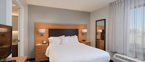 A hotel room with a large bed, bedside tables, a TV, and a window with curtains.