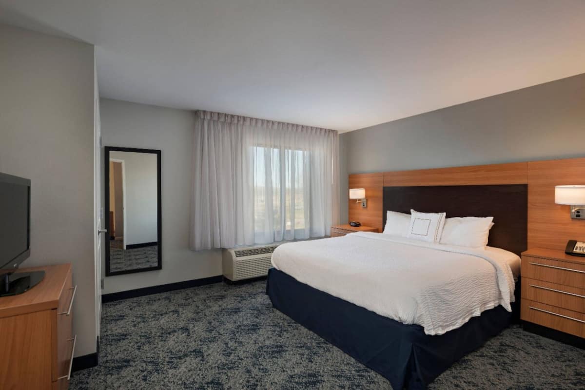 A hotel room with a large bed, a flat-screen TV, a mirror, a window with curtains, and a wooden headboard.