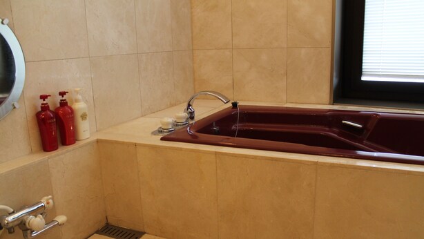 A bathroom with a bathtub, a mirror, and toiletries on the wall. - Hotel Nord Otaru (Otaru)