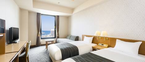 A hotel room with two beds, a desk with a TV, a small table, and a window with a view of the city.