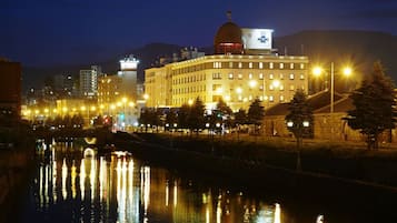 A nighttime view of a cityscape with a prominent building featuring a dome and multiple windows, reflecting lights on a calm river.